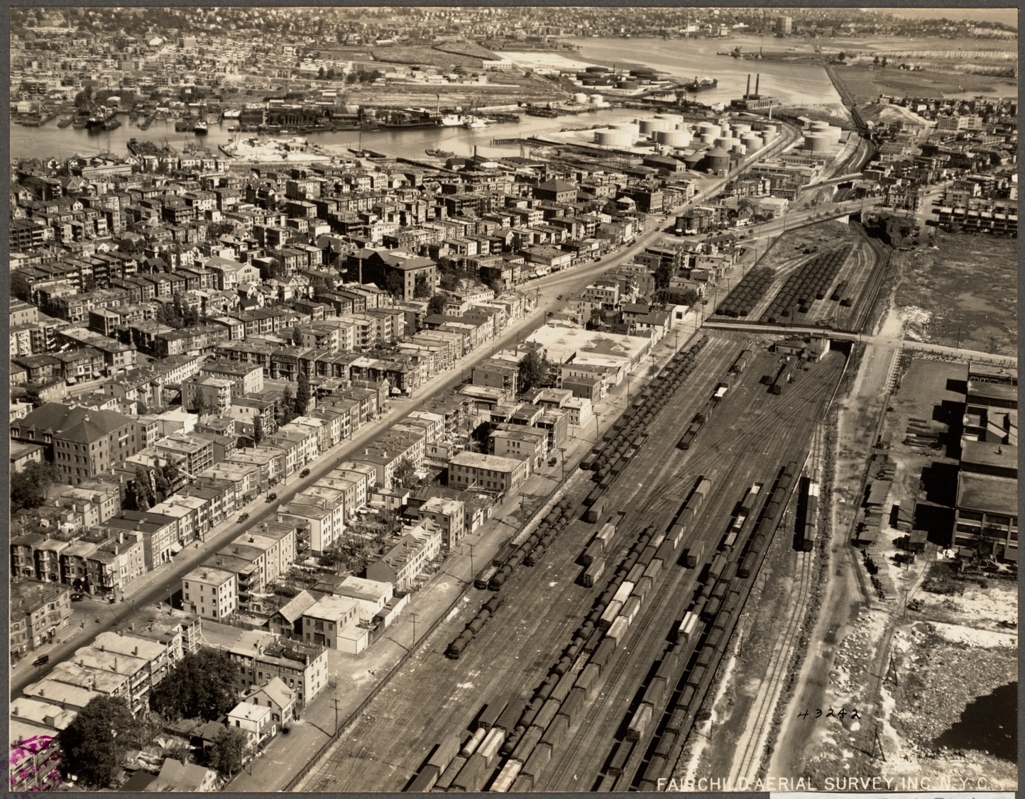 Aerial photograph of East Boston's working rail yard, freight cars running beside rows of neighborhood homes with the harbor beyond