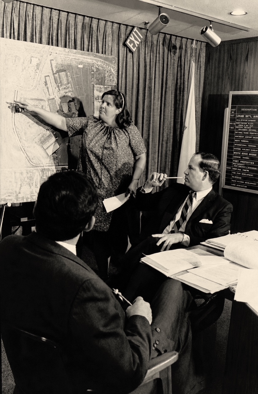 Mary Ellen Welch points to an aerial map of Logan Airport during a planning meeting, two officials looking on